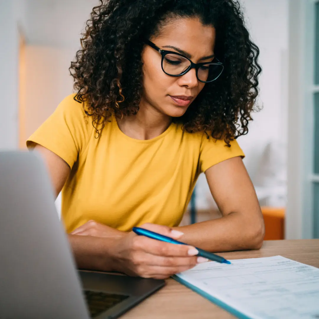 a woman in a yellow shirt at a desk holding a pen in her hand