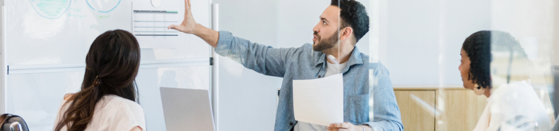 Three people in a boardroom looking at a white board