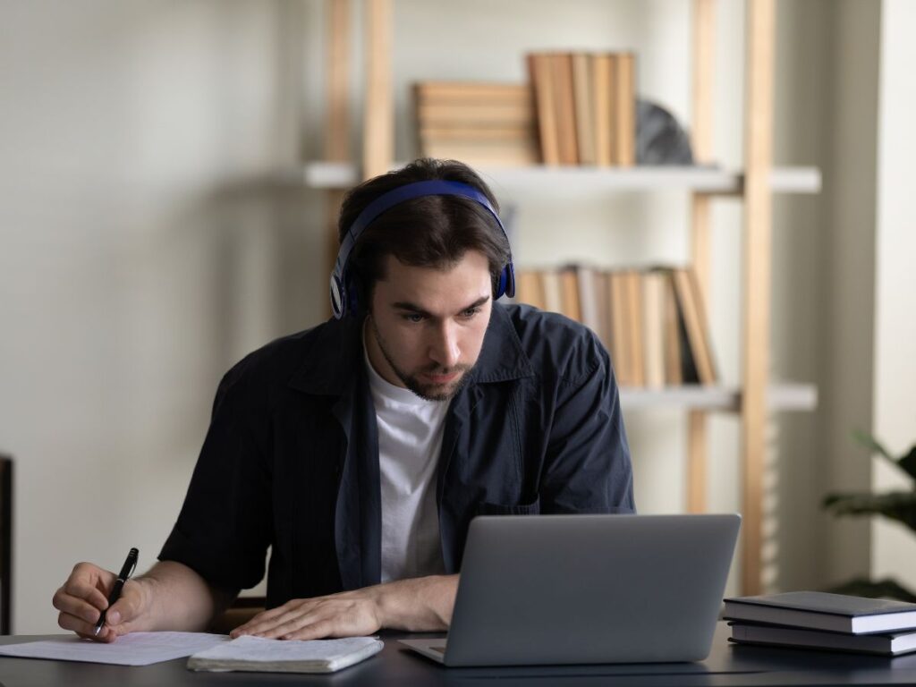 man sitting in front of a latop writing something on a piece of paper